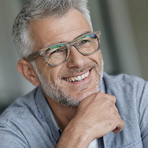 senior man with glasses smiling to show dental implants