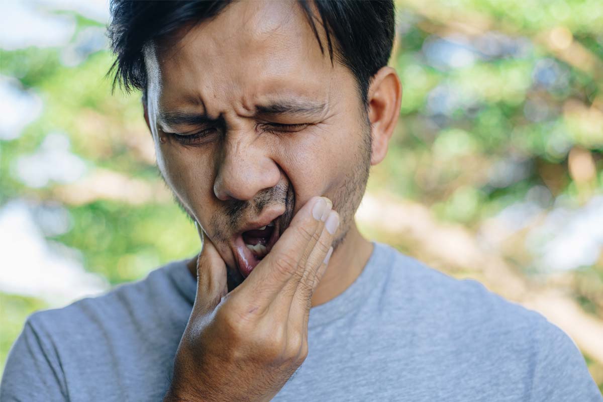 tooth-cavity-symptoms man wincing holding jaw from tooth cavity symptoms