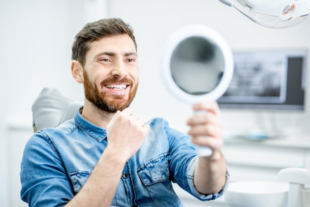 dental-bonding man smiling holding a mirror after dental bonding